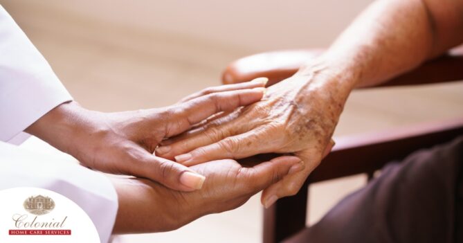 A pair of younger hands hold older ones, representing the compassionate care that a professional caregiver can provide.