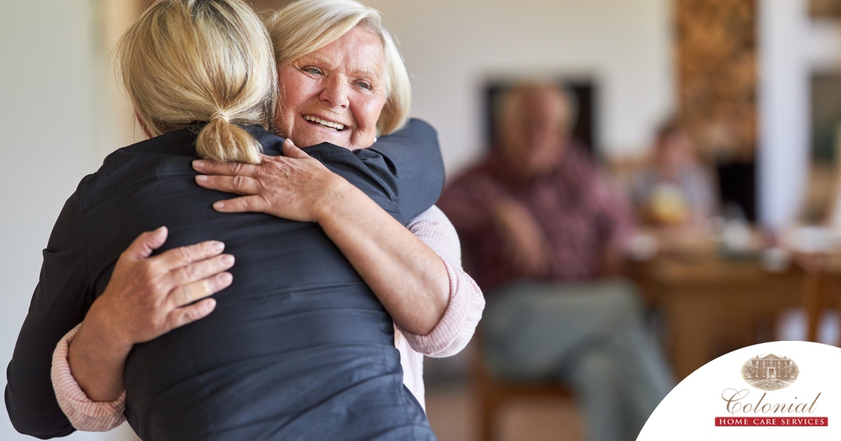 An older woman smiles as a younger woman visits her and hugs her, showing the effect that acts of kindness can have on senior loved ones.